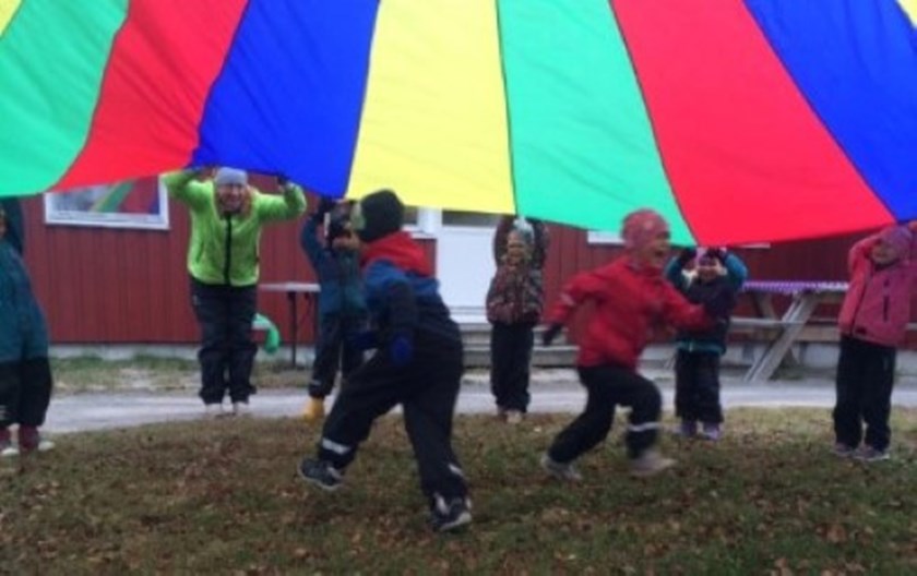 Bild av barn som glatt leker utomhus under ett flerfärgat tygstycke