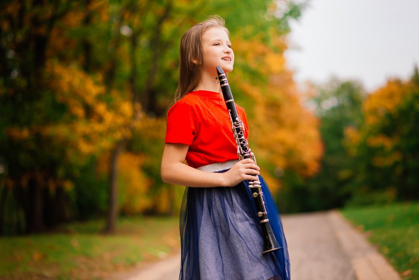 Ung tjej med klarinett på skogsbilväg en höstdag.