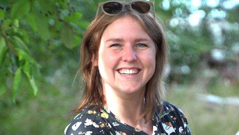 En leende glad Kristina Wikholm i sommargrönskande miljö.