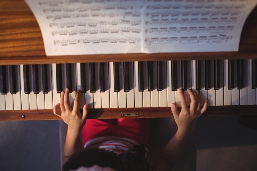 Flicka läser noter och har sina händer på pianotangenter.